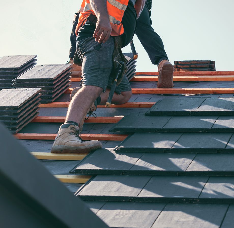 A roofer in hi-vis laying slate tiles on a pitched roof